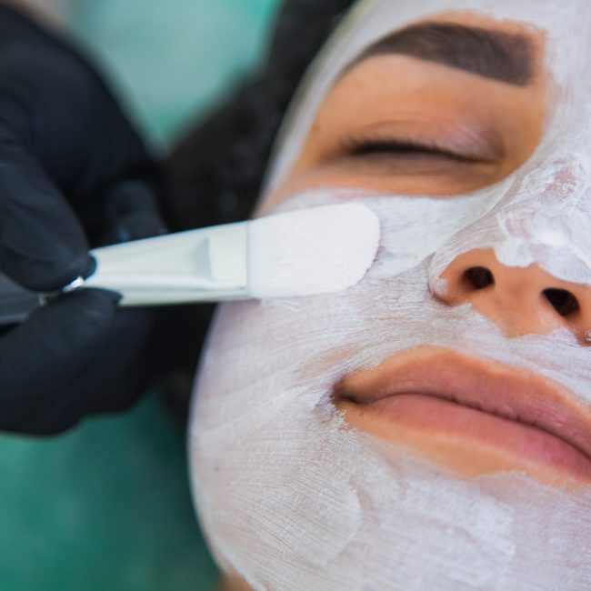 Closeup of woman face in white clay mask procedure in beauty salon. Face peeling mask, spa beauty treatment, skincare concept.